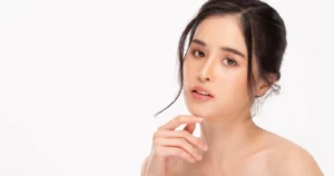 A woman with a neutral expression and a messy bun poses with her hand on her chin against a white background for Skin Booster in Mississauga.